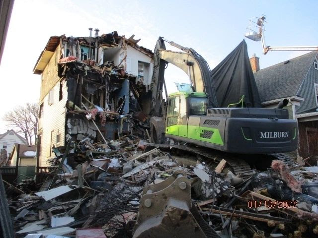 Excavator demolishing a building amidst rubble and debris.